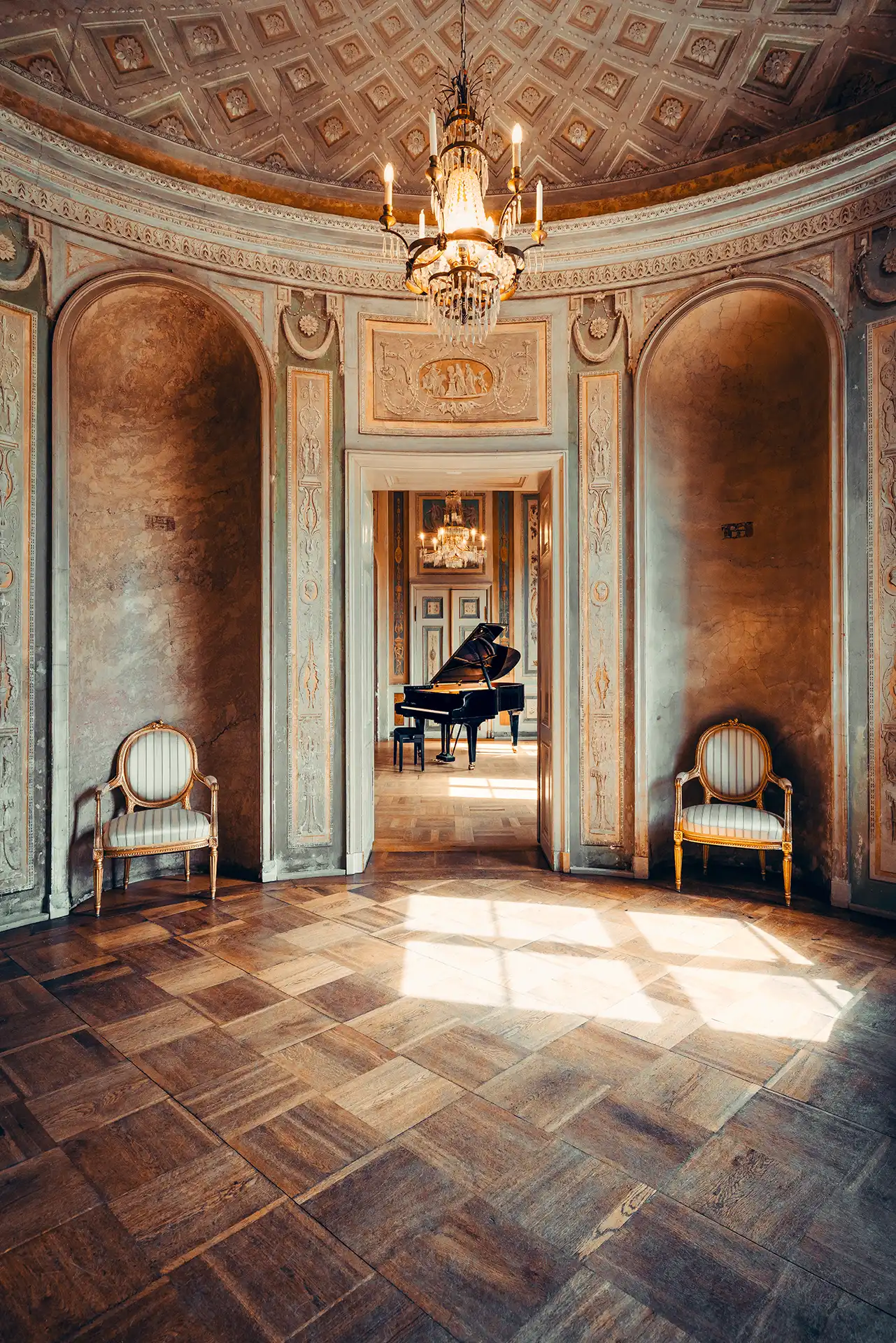 Der Rundsaal im Palais Lichtenau mit Kronleuchter, Stuhlpaar und einem Flügel im Nebenraum